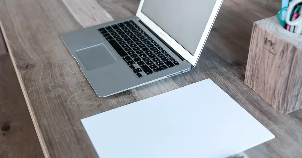 Notebook aberto ao lado de uma folha em branco sobre mesa de madeira, cena para sites para escrever texto ao contrário
