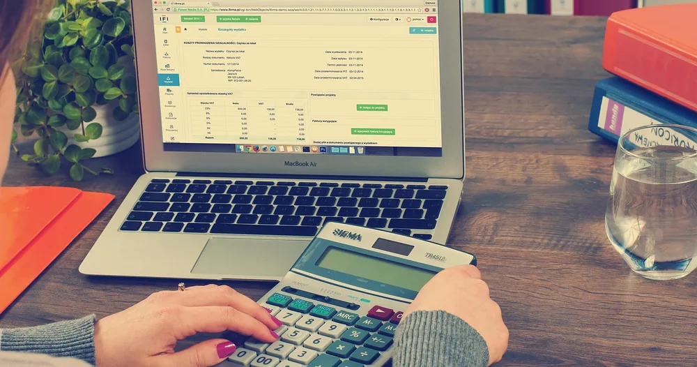 Pessoa usando calculadora ao lado de notebook com planilha de contabilidade